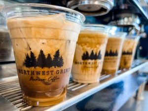 four iced coffee cups filled with lattes sitting on an espresso machine at Northwest Grind