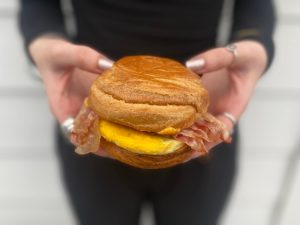 a woman holding a bacon breakfast sandwhich