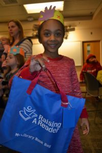 young girl holding a blue Child Care Action Council reading bag
