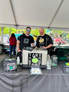 two men standing behind the Tart Hard Cider booth at Winterfest