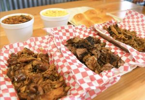 The Family Pack at Flaming Pig BBQ comes with a pound of pulled pork, a pound of chopped brisket, and a pound of pulled chicken. In addition, you get two pints of your favorite sides, your choice of bread and barbecue sauce sitting on a table