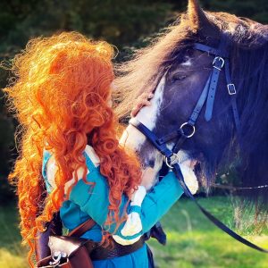 girl dressed as Merida from Disney's BRAVE with her hands on the nose and face of a horse wearing a bitless bridle