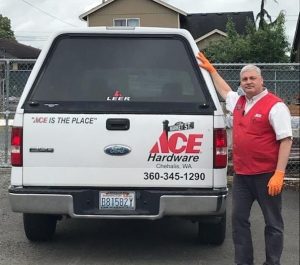 man in an ACE Hardware vest standing at the back of a white ACE Hardware pickup truck