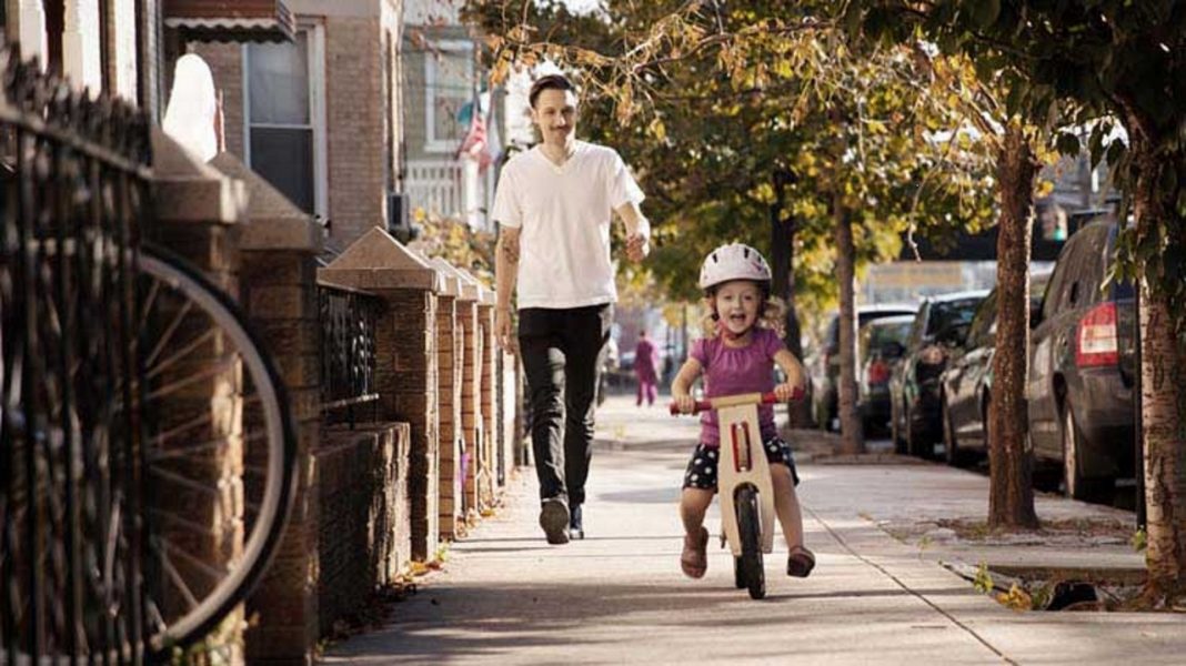 man walking on a sidewalk with a young girl on a bicycle
