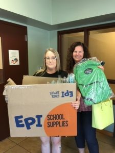 two women holding a cardboard box and bags full of school supplies