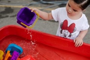 a child pouring water out of a container into a bigger one