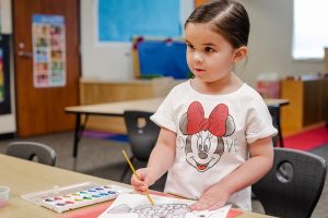 little girl standing at a desk with a pencil in her hand