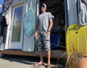 Mark Lewis standing by his surf lesson and rental business in Wesport