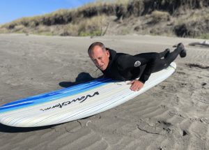 man lying on his belly on a surfboard on the beach at Wesport