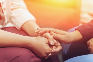 two people sitting, one with their fingers crossed the other's hand on top