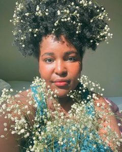 Eunice Ndungu of Bloom + Brew with flowers in her hair and in front of her