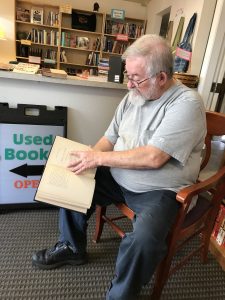 Murlin Varner sitting in a chair with an old book at Turtleman Used Books in Olympia