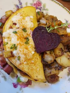 plate with an omelette, grilled breakfast potatoes and a slice of beet in the shape of a heart