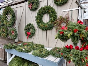 a large selection of fresh-greenery wreaths hanging on a barn door at the Olympia Farmers Market