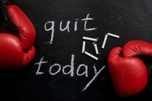 Words 'quit today' on a black chalkboard with boxing gloves lying on it
