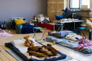 shelter beds set up in a large room with a few toys and camp chairs