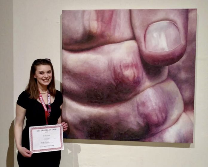 Trisha Hall standing next to her painting of a fist up close