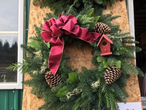 a Christmas wreath with a red bow and pinecones hanging on a door