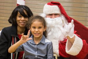 santa with a girl on his lap and her mom next to him, girl and santa are signing