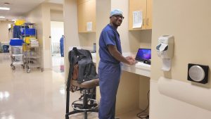 Dr Lamour standing at a laptop in his scrubs at Oly Ortho