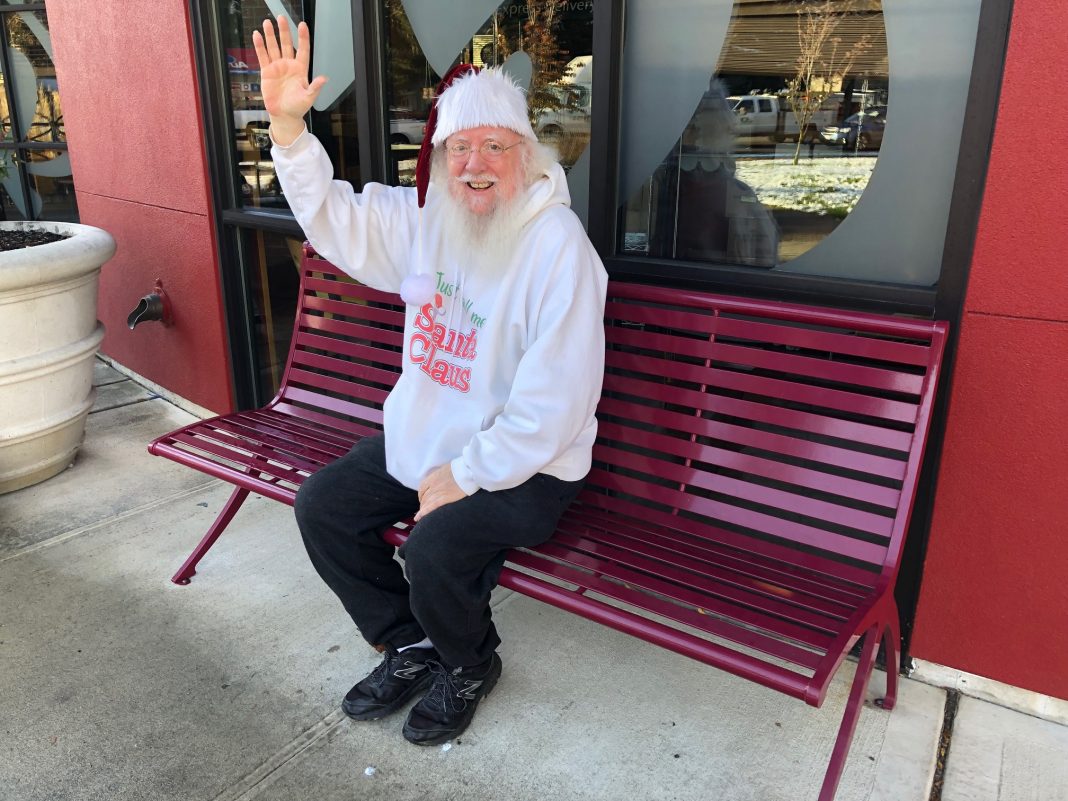 Santa Bob in a santa hat sitting on a bench, waving
