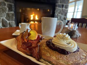 buckwheat pancakes, bacon and a cup of coffee on a table with a fireplace in the background at The Port Ludlow Resort