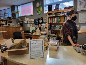 Evergreen College student working at the checkout at Orca's Books with a cat in a box on the counter