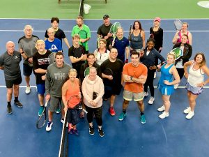 large group of people standing on tennis court and steam athletic club
