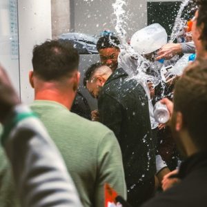 The Evergreen State College men's basketball team in the locker room pouring water over their interim head coach in celebration