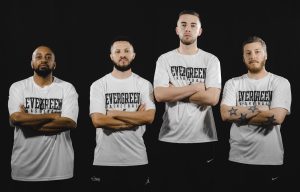 Four members of the Evergreen State College post with arms folded against their chest in white shirts on a black background
