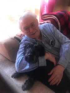 Harvey Drahos on a couch hugging his black dog