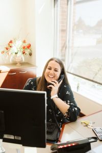 woman bank worker sitting at a desk with a computer and holding a phone to her ear.