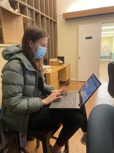 woman sitting in a room with face mask on and a laptop on her lap