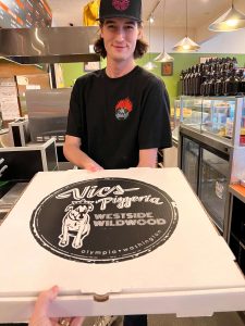 Avryn Reynolds, a shift manager at Vic's Pizzeria, hands over a freshly baked pepperoni pizza, all boxed up and ready to be enjoyed by a lucky customer.