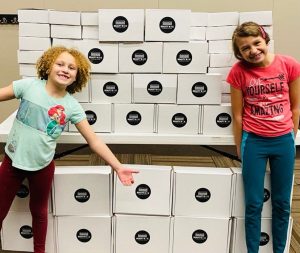 two kids standing in front of a bunch of Compelled to Care boxes