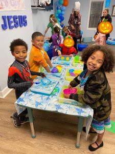 a group of kids doing crafts at a table with more kids inthe background