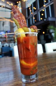 a fancy cocktail in a tall glass with bacon and olives at Uptown Lounge