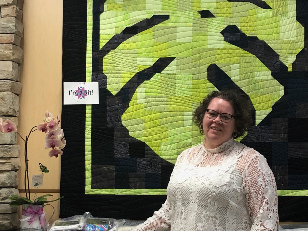 Stitches Quilt & Craft owner Adrienne Wilkie stands before a striking leaf quilt in her new shop in Olympia.