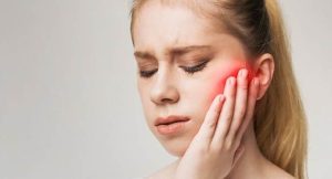 woman holding her jaw with her hand because it hurts, jaw is highlighted red