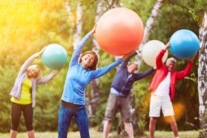 senior citizens stretching in a park while holding large yoga balls above their heads