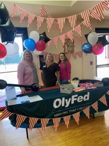 Melissa Kirkeby at an OlyFed table at an event (standing with two other women)