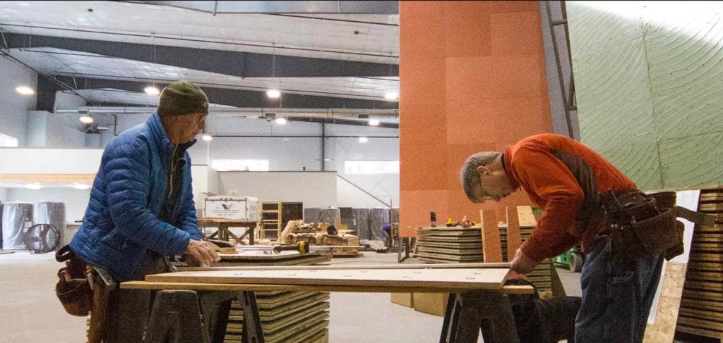 two people working on on the construction of a climbing wall with a big piece of wood on two saw horses