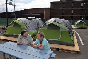 two people talking at a picnic table with tents in the background