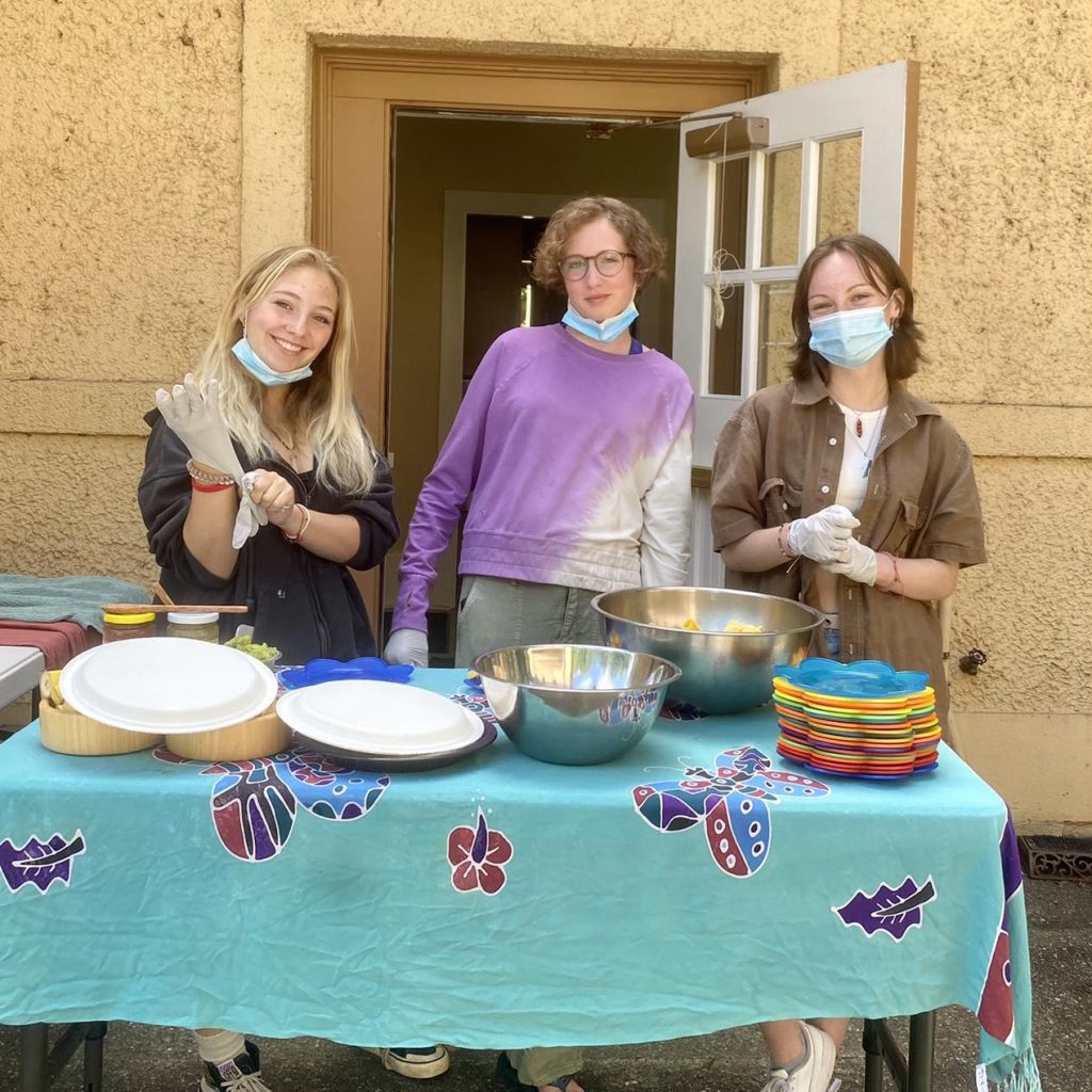 Three teenage girls smiling behind a table with bowls of food and serving plates