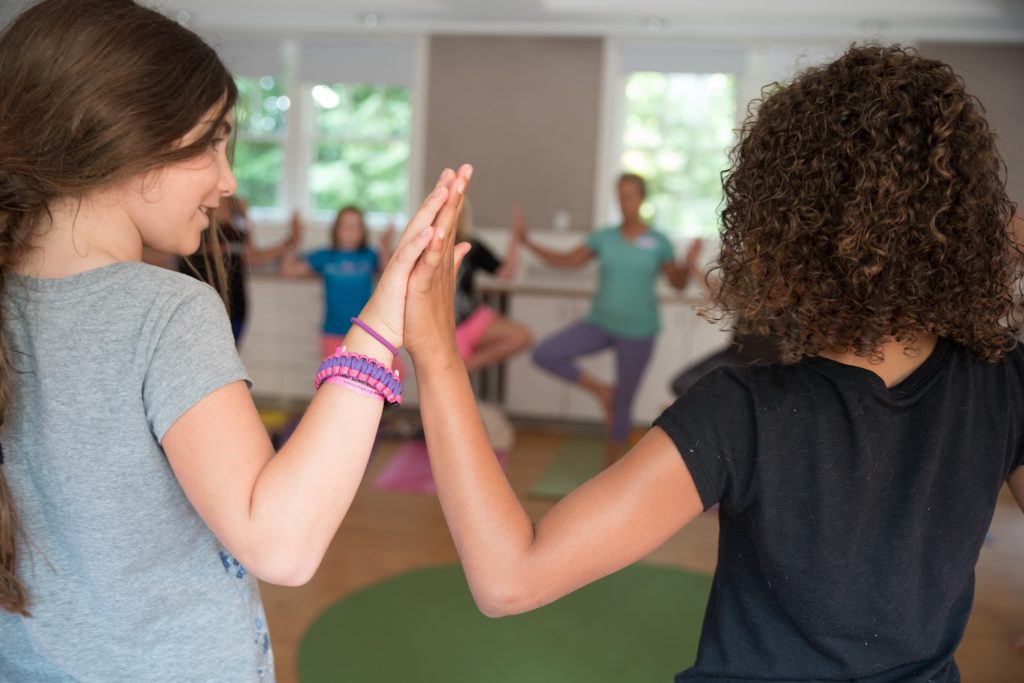 Two girls touching their palms together while doing yoga