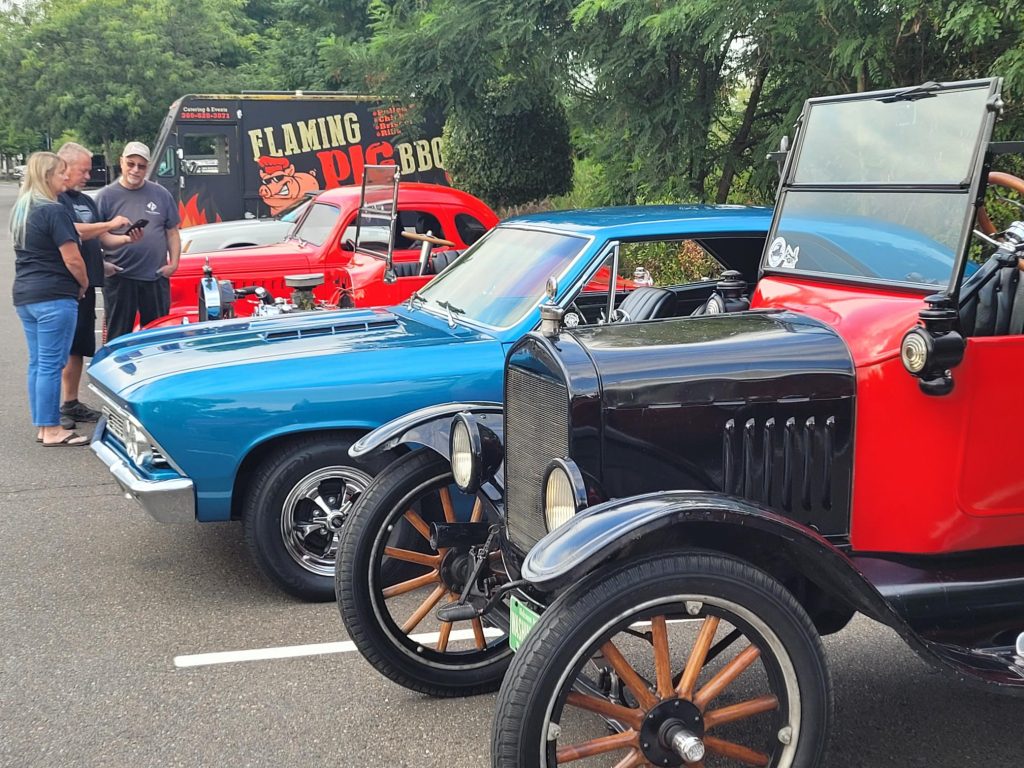 a row of vintage and classic cars in a parking lot with people looking at them