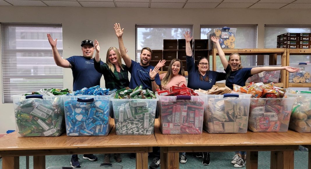 A group of people putting food into backpacks for All Kids Win