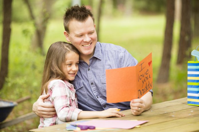 Daughter shows dad handmade Father's Day card. Outdoors. Child, parent.