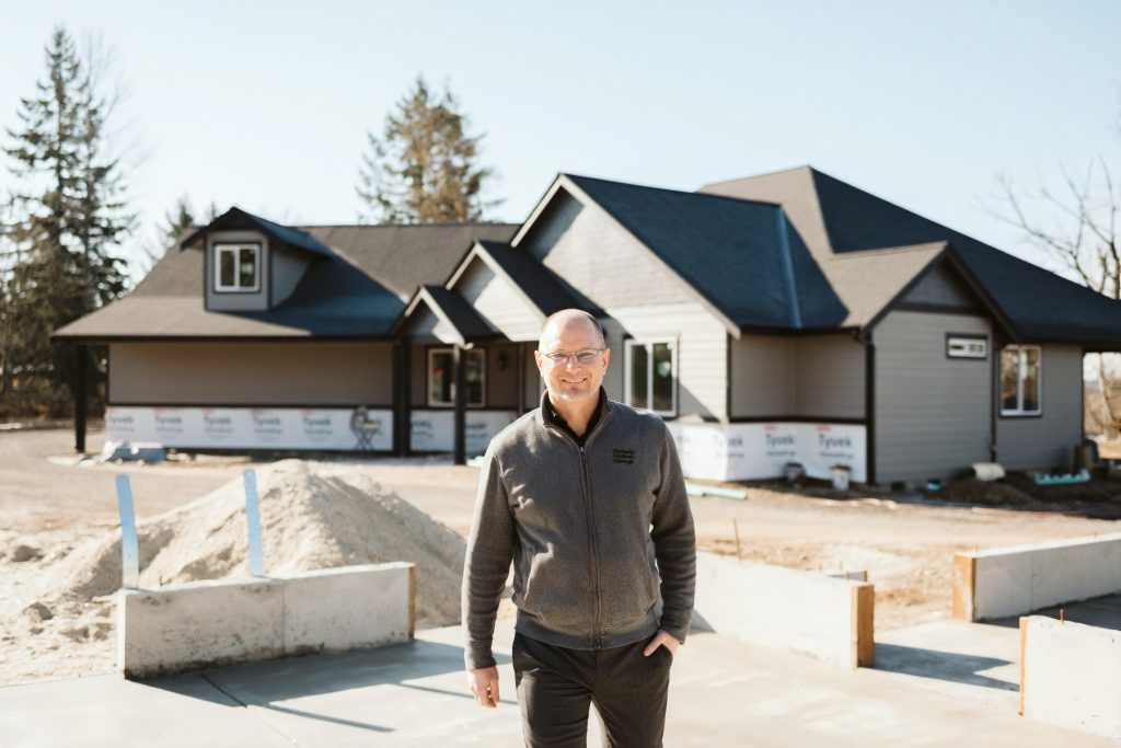 a guy smiling in front of a house that is being built