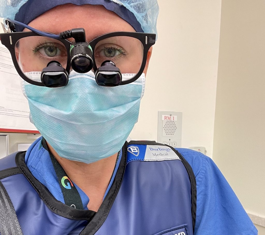 Christine Hammer in her scrubs with a face mask, head cap and glasses with magnifiers